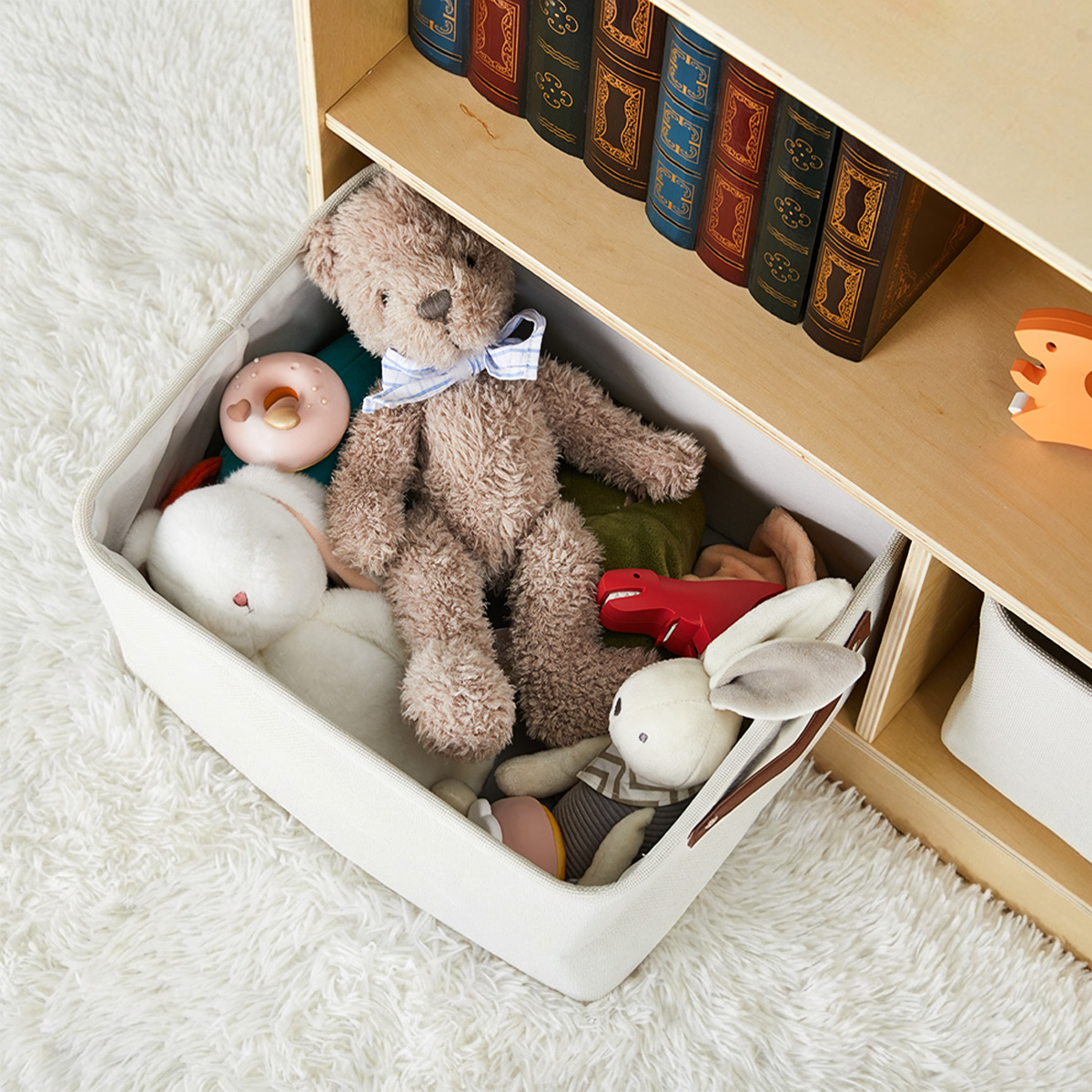 Removable fabric storage bin filled with plush toys beside Montessori shelf